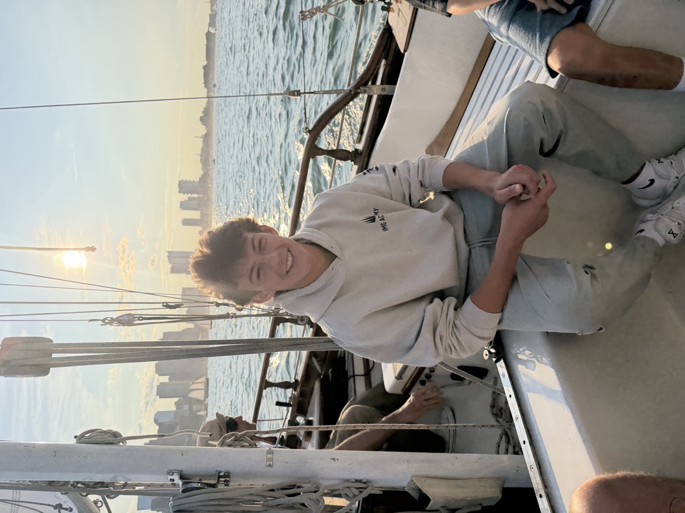 Portrait of Alex smiling on a sailboat at sunset with the city skyline behind him