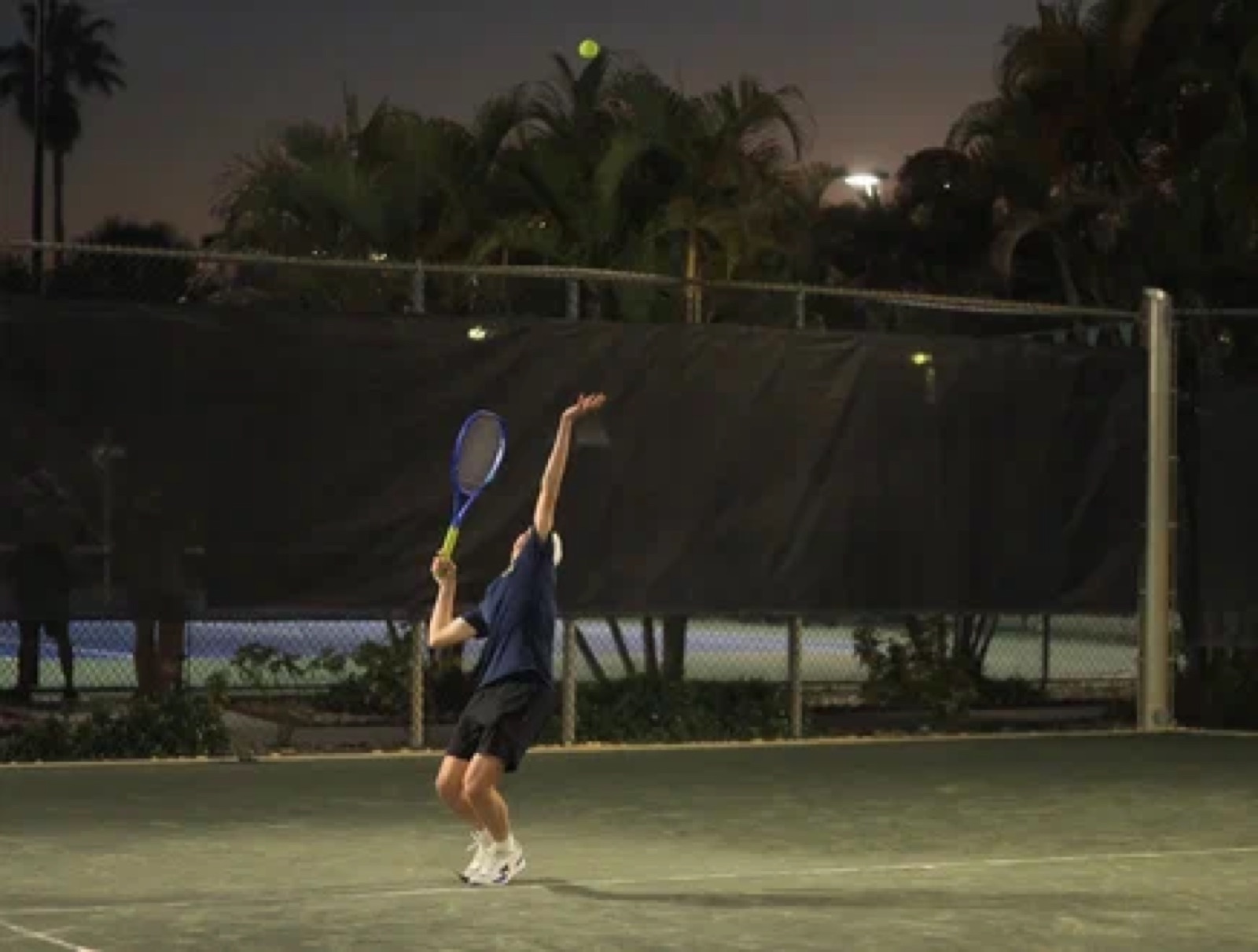 Alex serving during a night tennis match